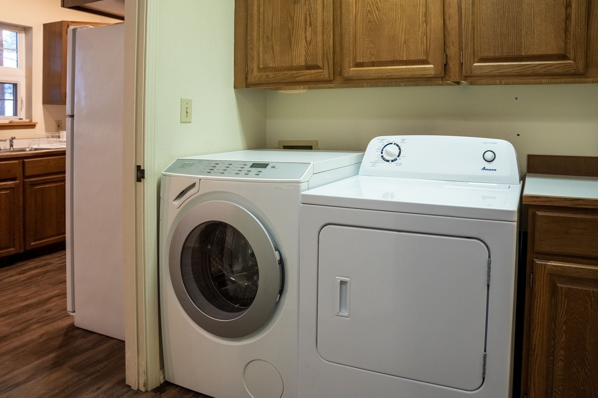 A front-loading washing machine in a kitchen with wooden cabinets and a refrigerator.