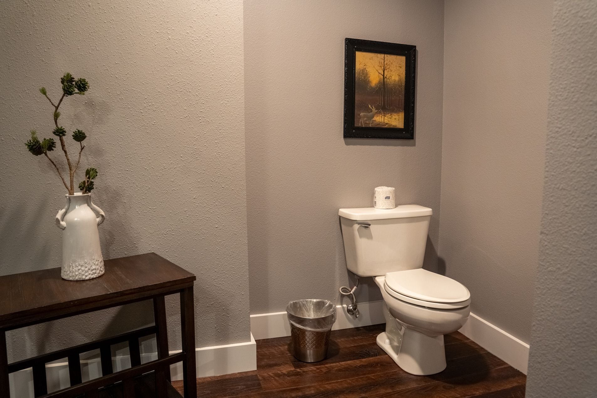 Un baño con un inodoro, un cubo de basura y un cuadro en la pared.
