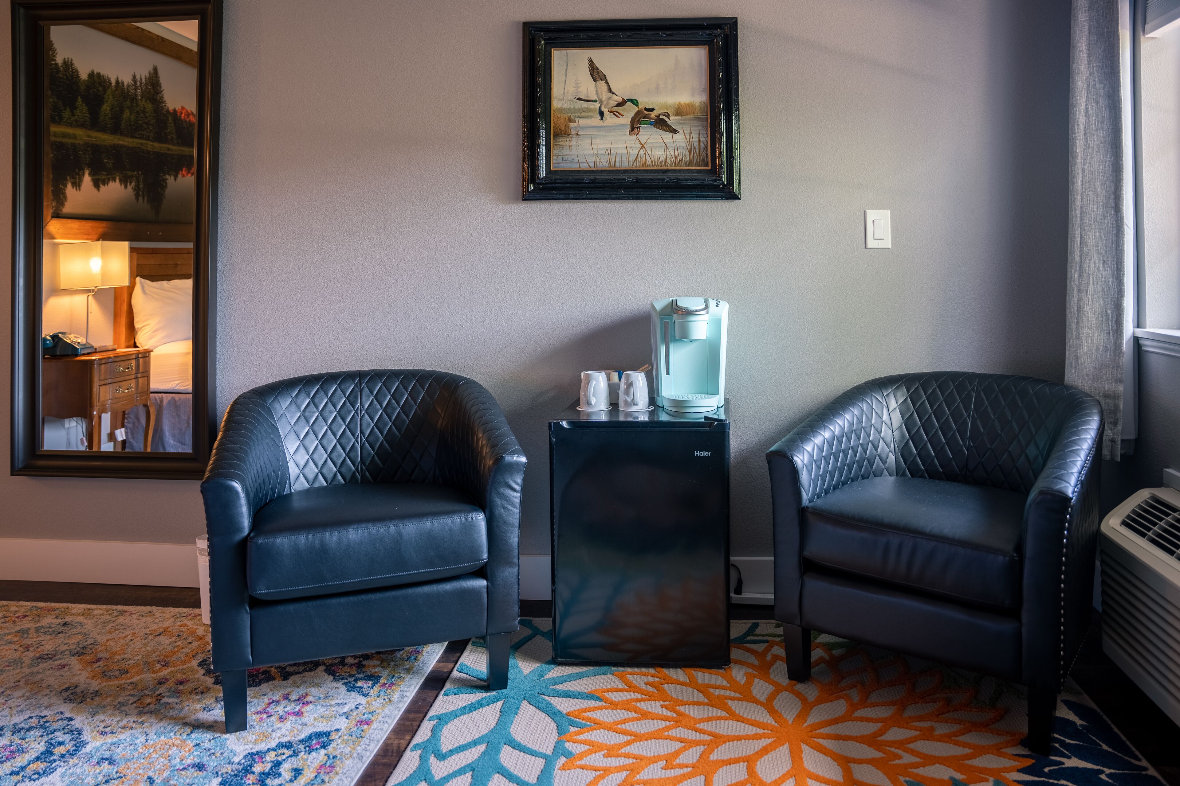 Une chambre d’hôtel avec deux fauteuils en cuir, une machine à café, un tableau encadré représentant des canards et un tapis à motifs.