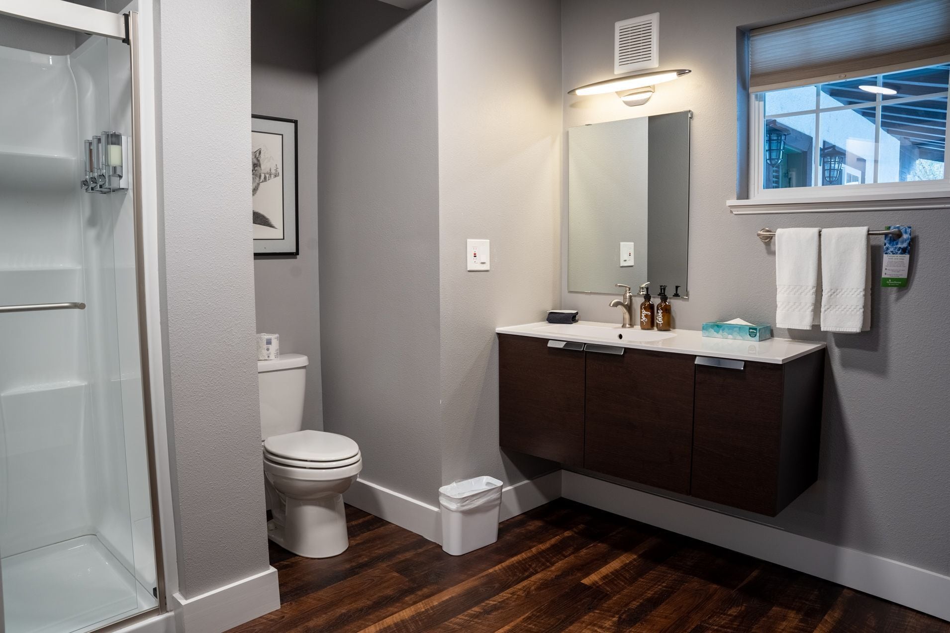 A modern bathroom with a white toilet, a dark wood vanity, a large mirror, and a window with a view.