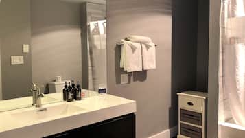 Un baño con un lavabo blanco, un espejo, un perchero con toallas, una botella de loción y un armario pequeño.