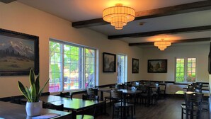 Un'ampia sala da pranzo con numerosi tavoli e sedie, grandi finestre che lasciano entrare la luce naturale e lampadari a soffitto.