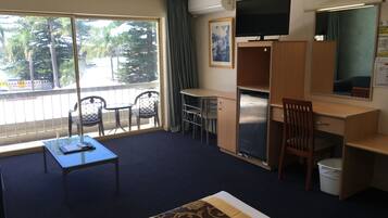 Habitación de hotel con cama, escritorio, silla, televisión y balcón con sillas.