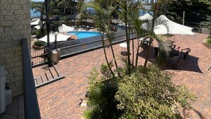 A pool area with a clear blue sky, surrounded by palm trees and a brick patio.
