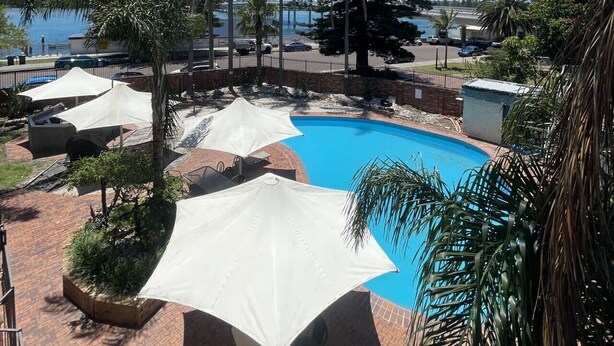 A pool area with umbrellas, palm trees, and a view of the sea.