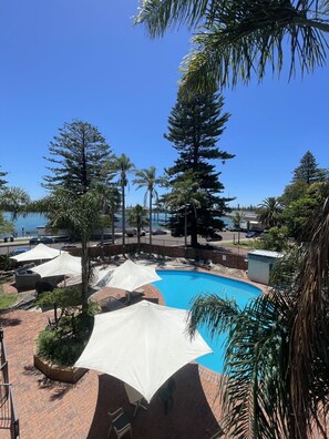 Zona de piscina con sombrillas, palmeras y vista al mar.