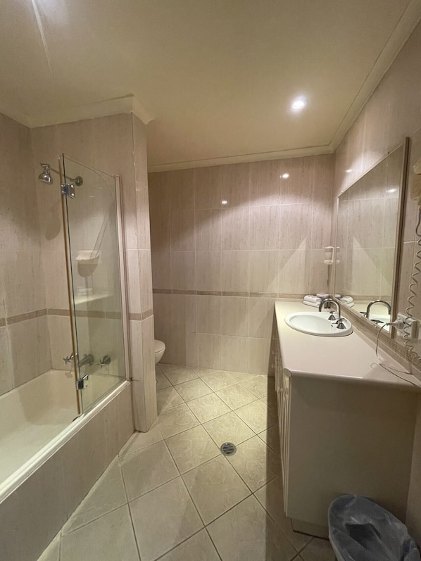Un baño moderno con ducha envuelta en vidrio, inodoro y lavamanos con espejo.