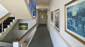 A hallway with a staircase, framed pictures on the walls, and a carpeted floor.