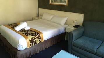 A hotel room with a neatly made bed, a chair, a bedside table with a lamp, and a framed picture on the wall.
