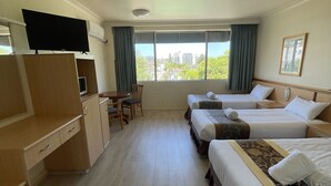 A hotel room with two beds, a desk, a chair, a television, and a window with a view of buildings.