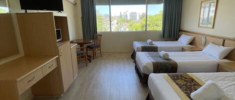 Une chambre d’hôtel avec deux lits, un bureau, une chaise, une télévision et une fenêtre donnant sur des immeubles.