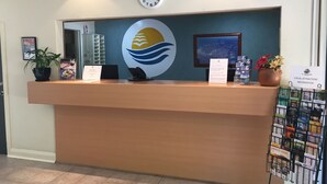 A reception desk with a clock, a framed picture, a potted plant, a sign, and a magazine rack.