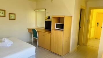 Habitación de hotel con cama, escritorio con computadora y microondas, una silla y un espejo.