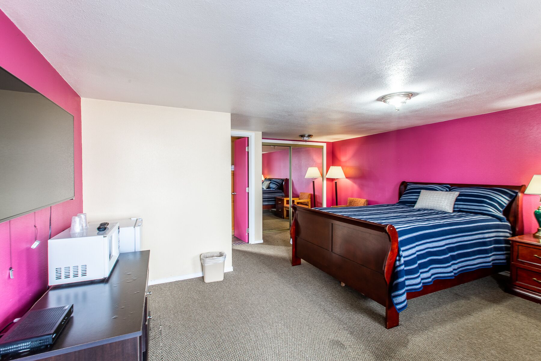 Habitación de hotel con cama, mesitas de noche, escritorio, espejo y puerta que da a otra habitación.