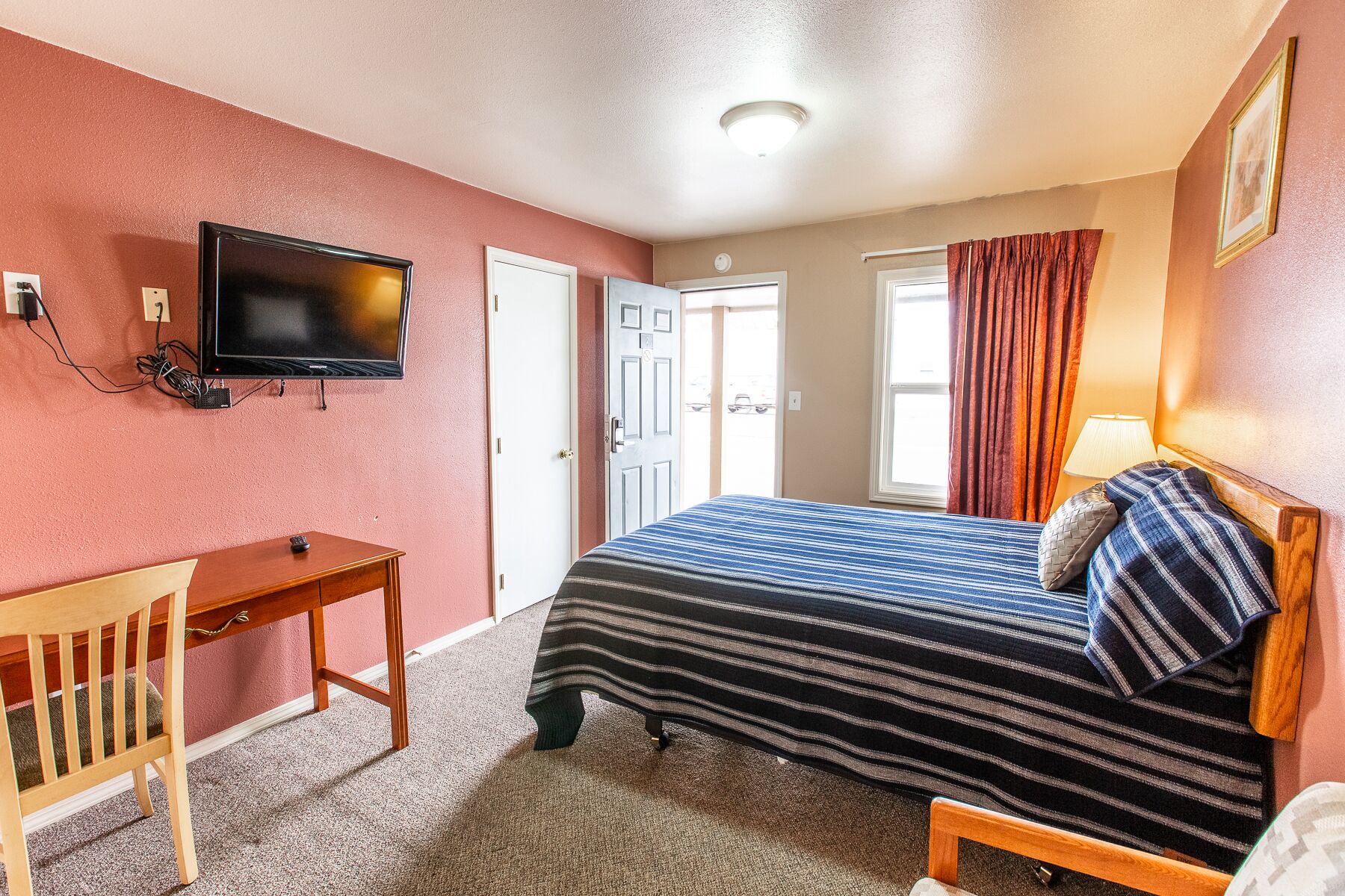 Habitación de hotel con cama, escritorio, televisor y ventana con cortinas.