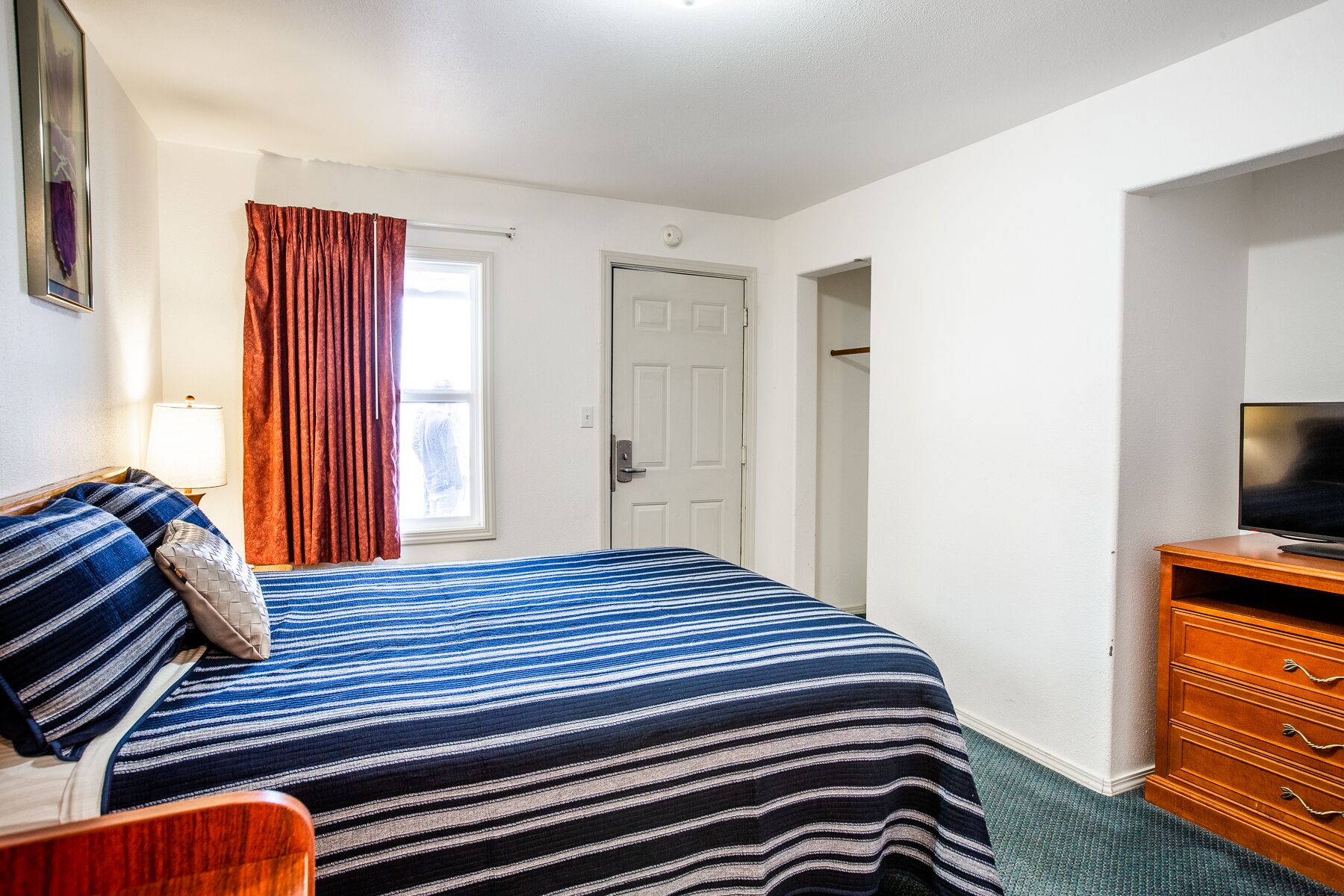 Una habitación de hotel con una cama, un televisor, un aparador y una puerta que da a otra habitación.