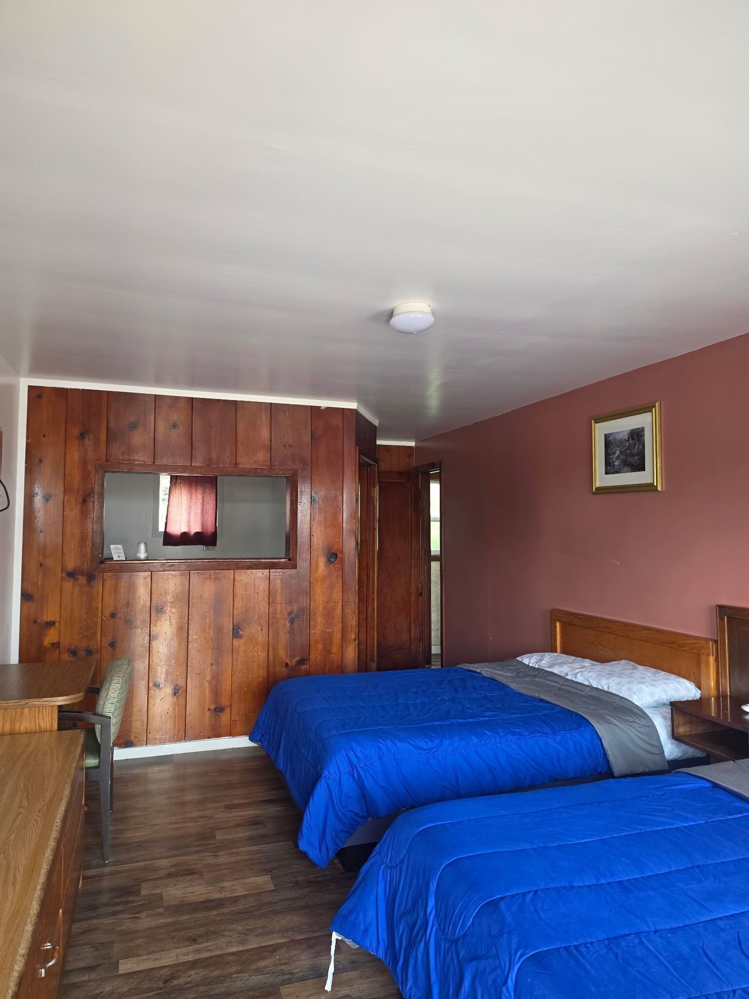 Une chambre avec deux lits, des murs recouverts de lambris en bois, un bureau et une chaise.