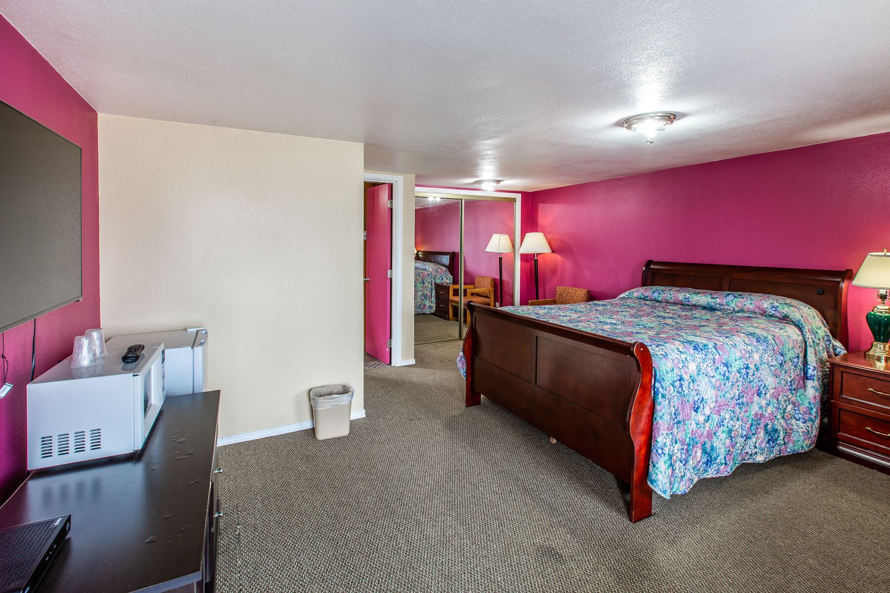 Une chambre d’hôtel avec un lit, une table de chevet, une lampe et un bureau équipé d’un ordinateur et de lunettes.