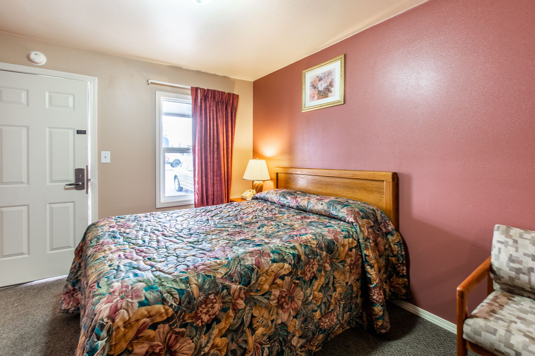 Una camera d'albergo con un letto, una sedia, una lampada e una finestra con tende.