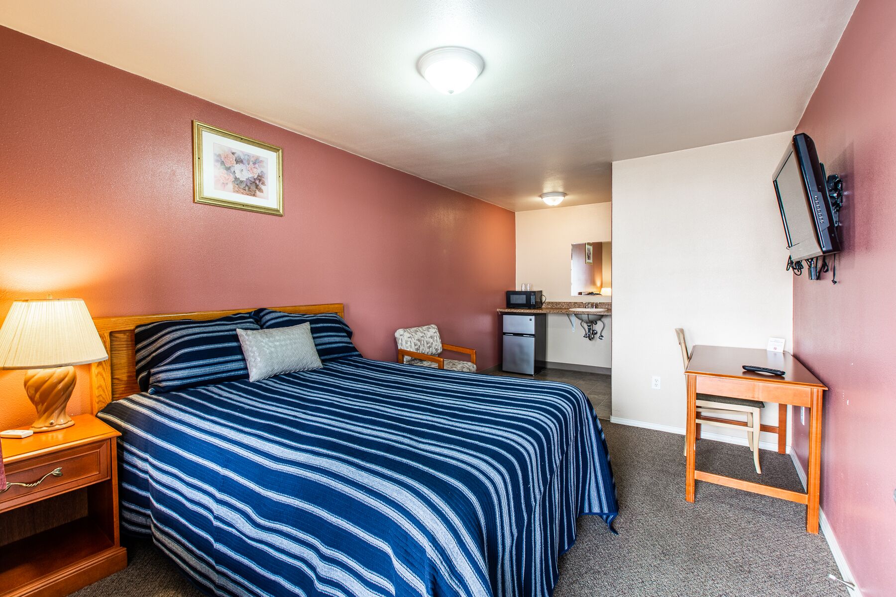 Een hotelkamer met een bed, een bureau, een stoel, een kitchenette en een televisie.