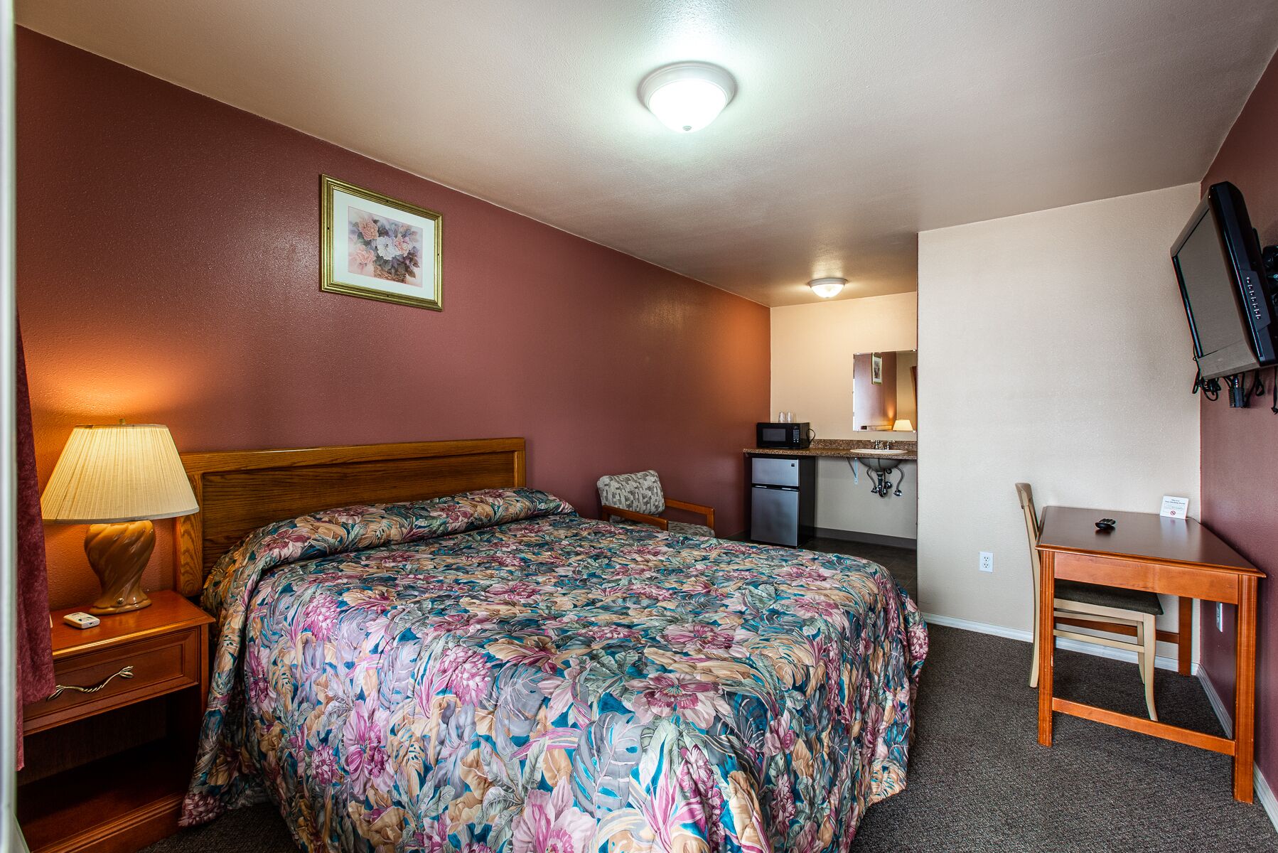 Una camera d'albergo con un letto, una scrivania, un angolo cottura e una televisione.