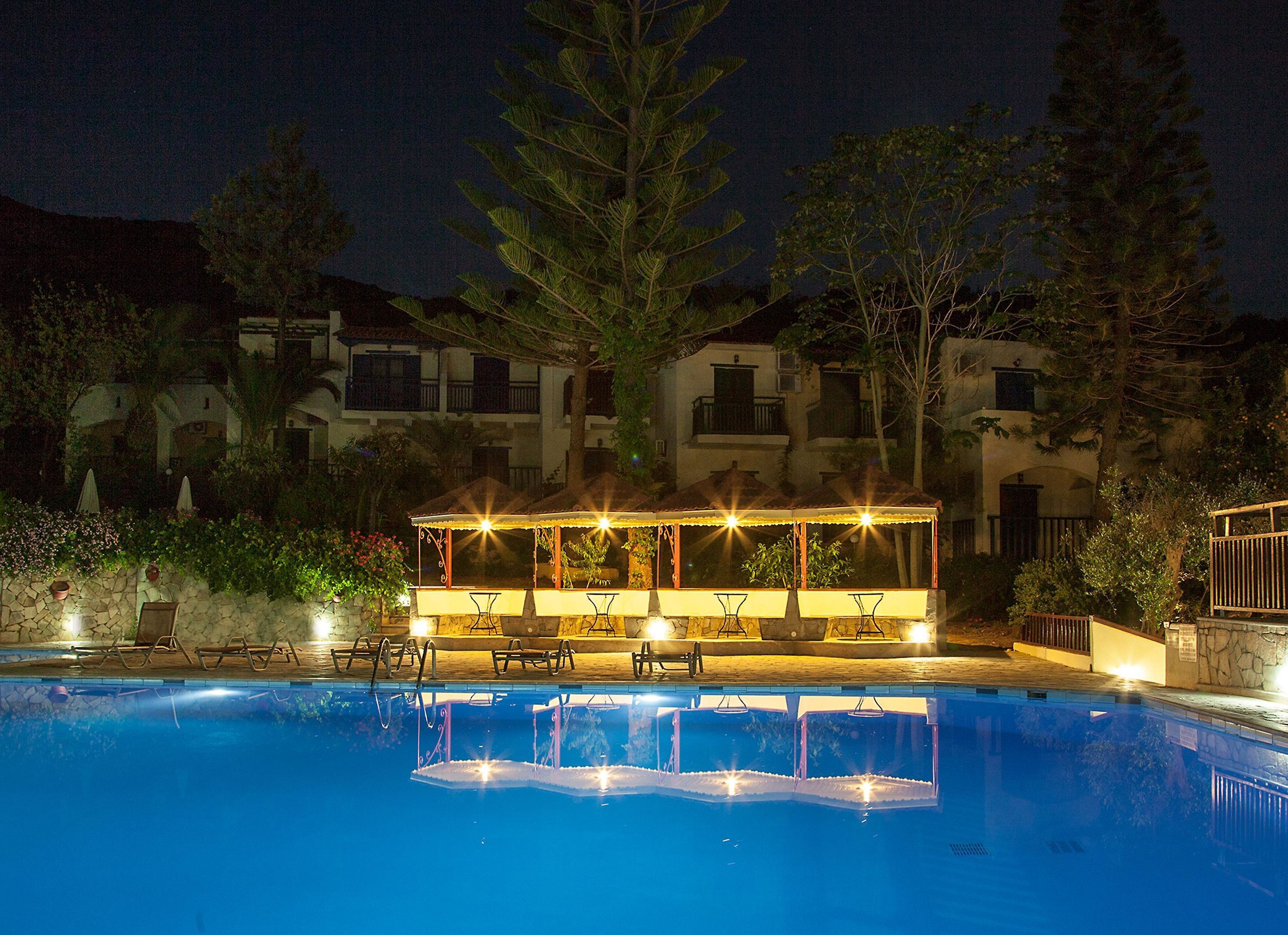 Ein Pool mit einer Sitzecke im Wasser und einem überdachten Pavillon bei Nacht.