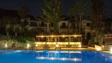 Ein Pool mit einer Sitzecke im Wasser und einem überdachten Pavillon bei Nacht.