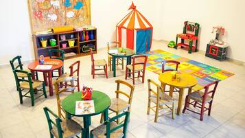 Ein Kinderspielzimmer mit Tischen, Stühlen, einem Spielzelt und einem farbenfrohen Teppich.