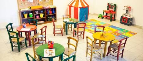 A children's playroom with tables, chairs, a play tent, and a colorful rug.