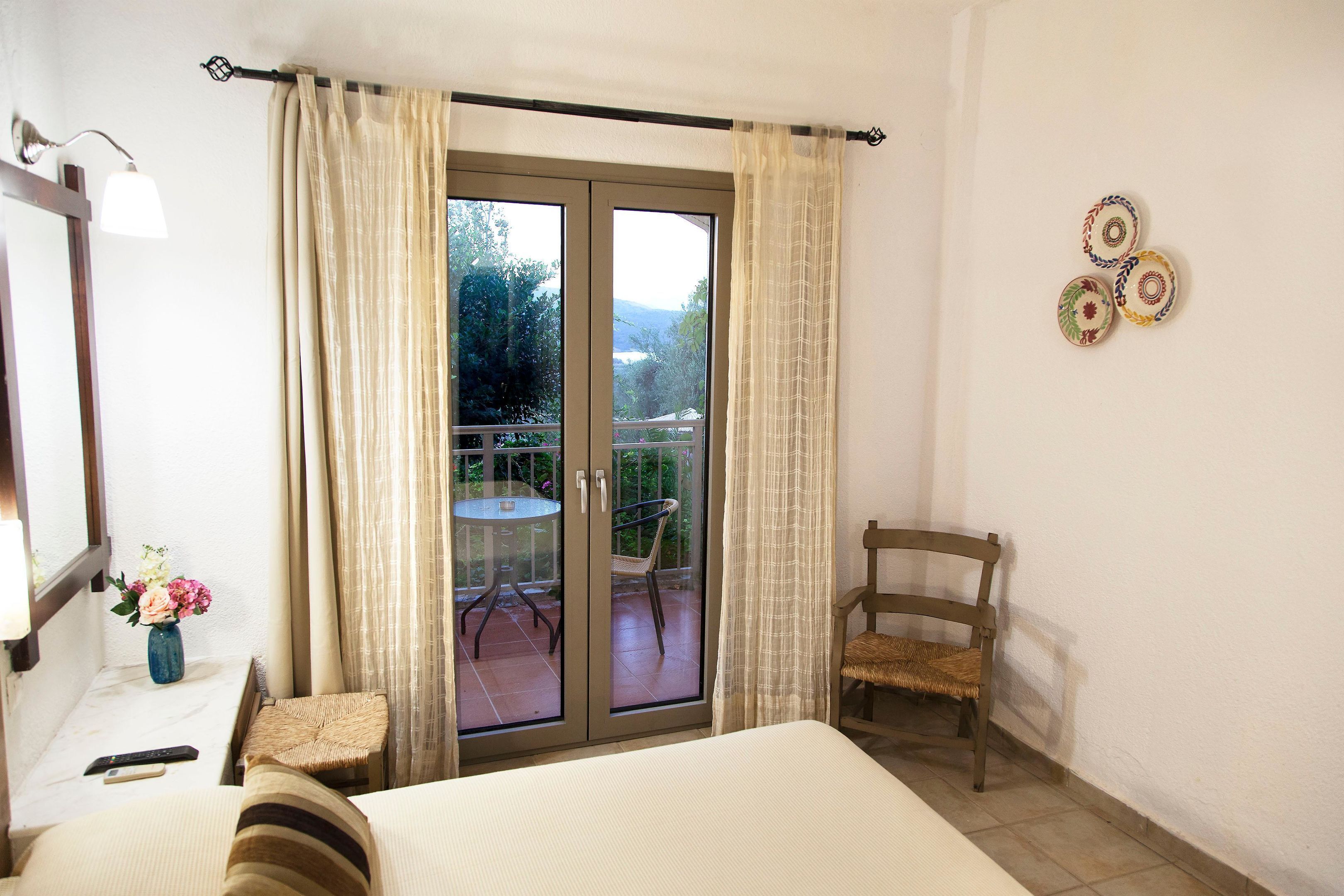 A bedroom with a bed, a chair, a small table with a vase of flowers, and a balcony with a table and chairs.