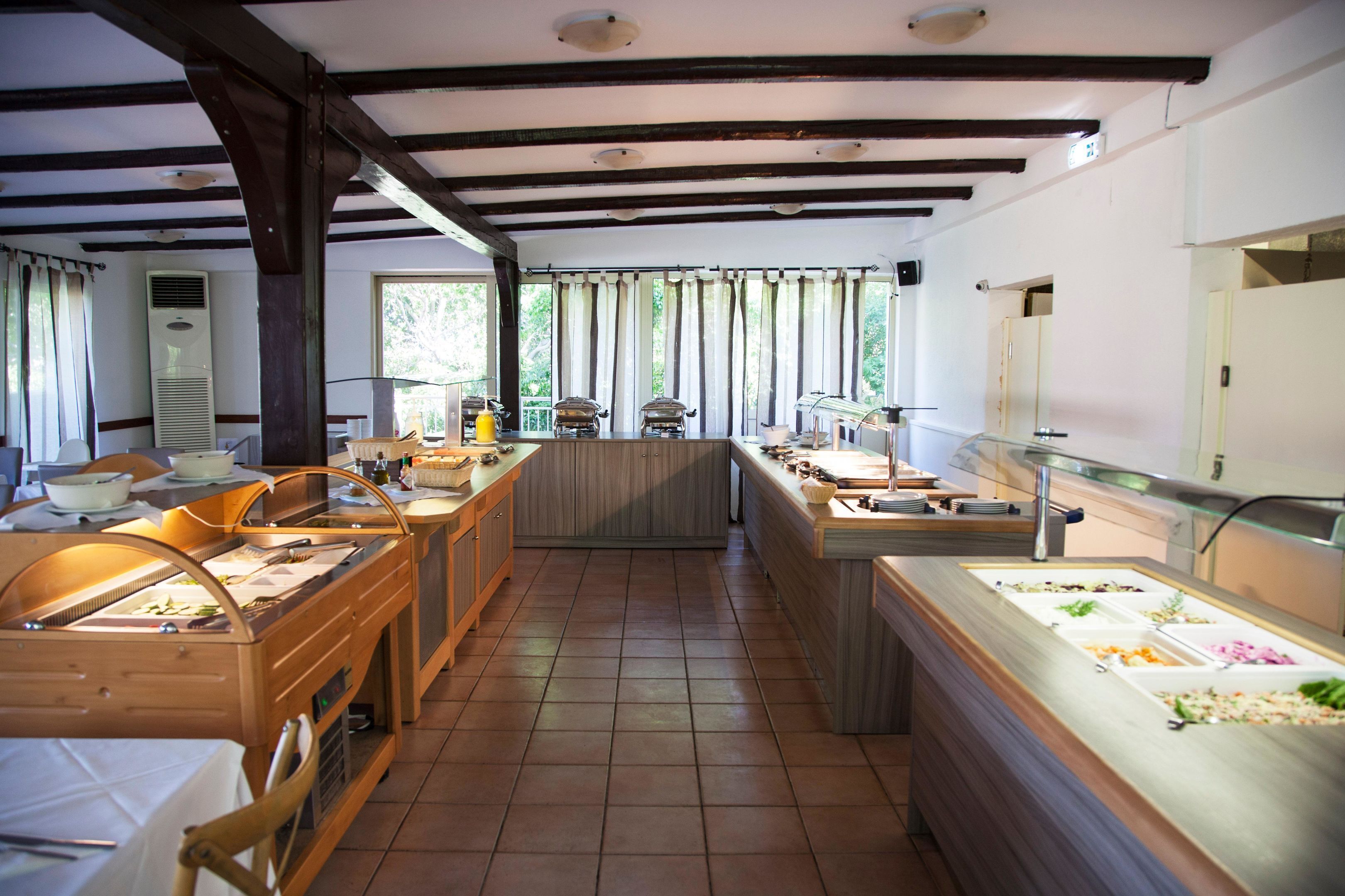 A kitchen with wooden tables, a buffet counter, and a large window with curtains.