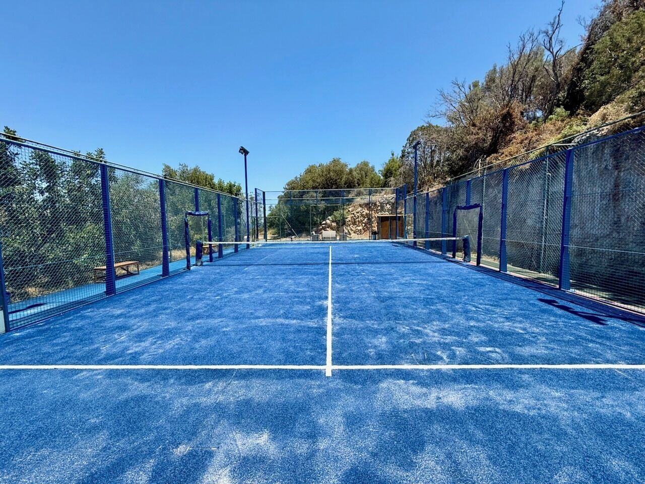 An outdoor tennis court with blue flooring and chain-link fencing.