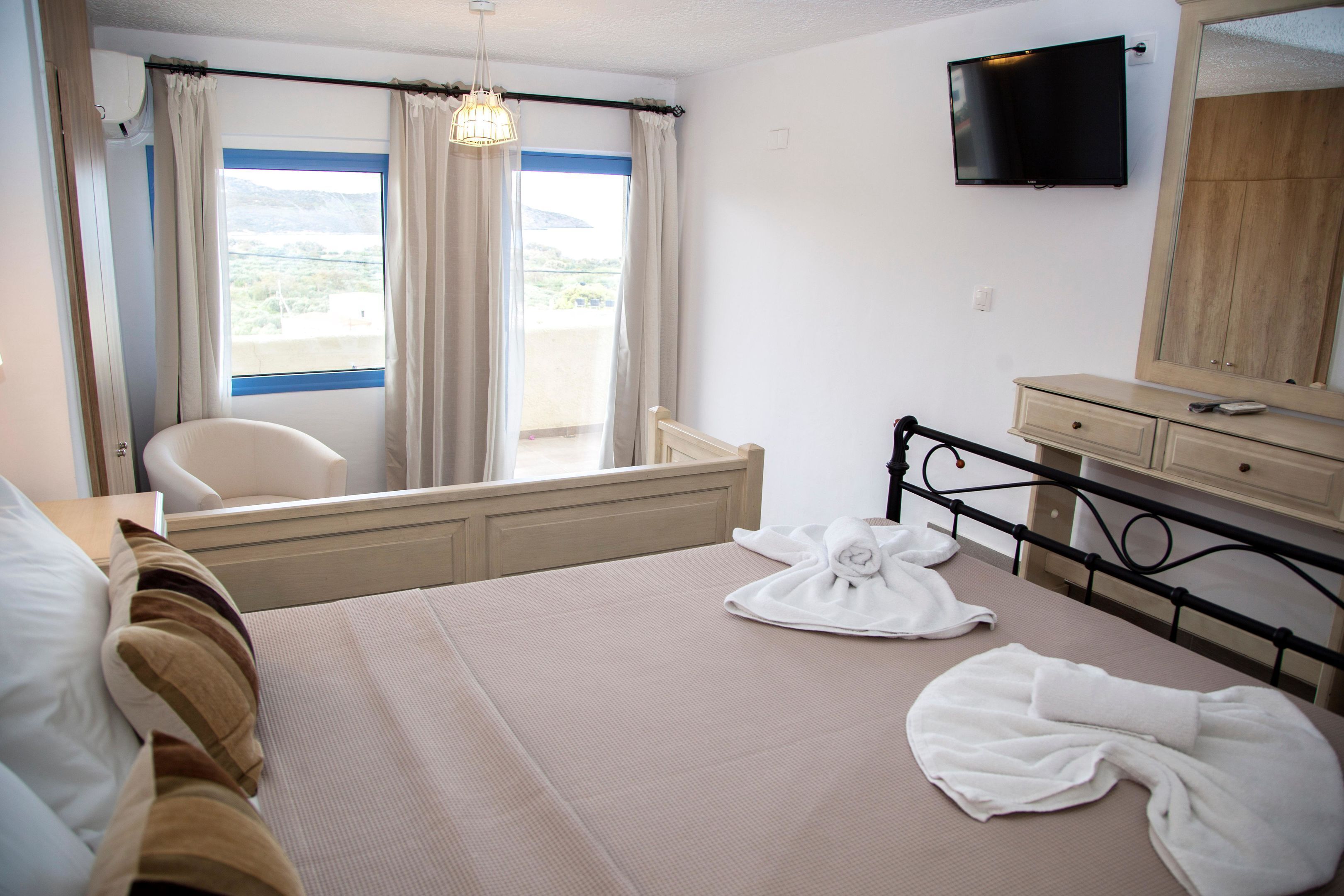 A hotel room with a bed, a chair, a TV, a mirror, and a window with curtains.