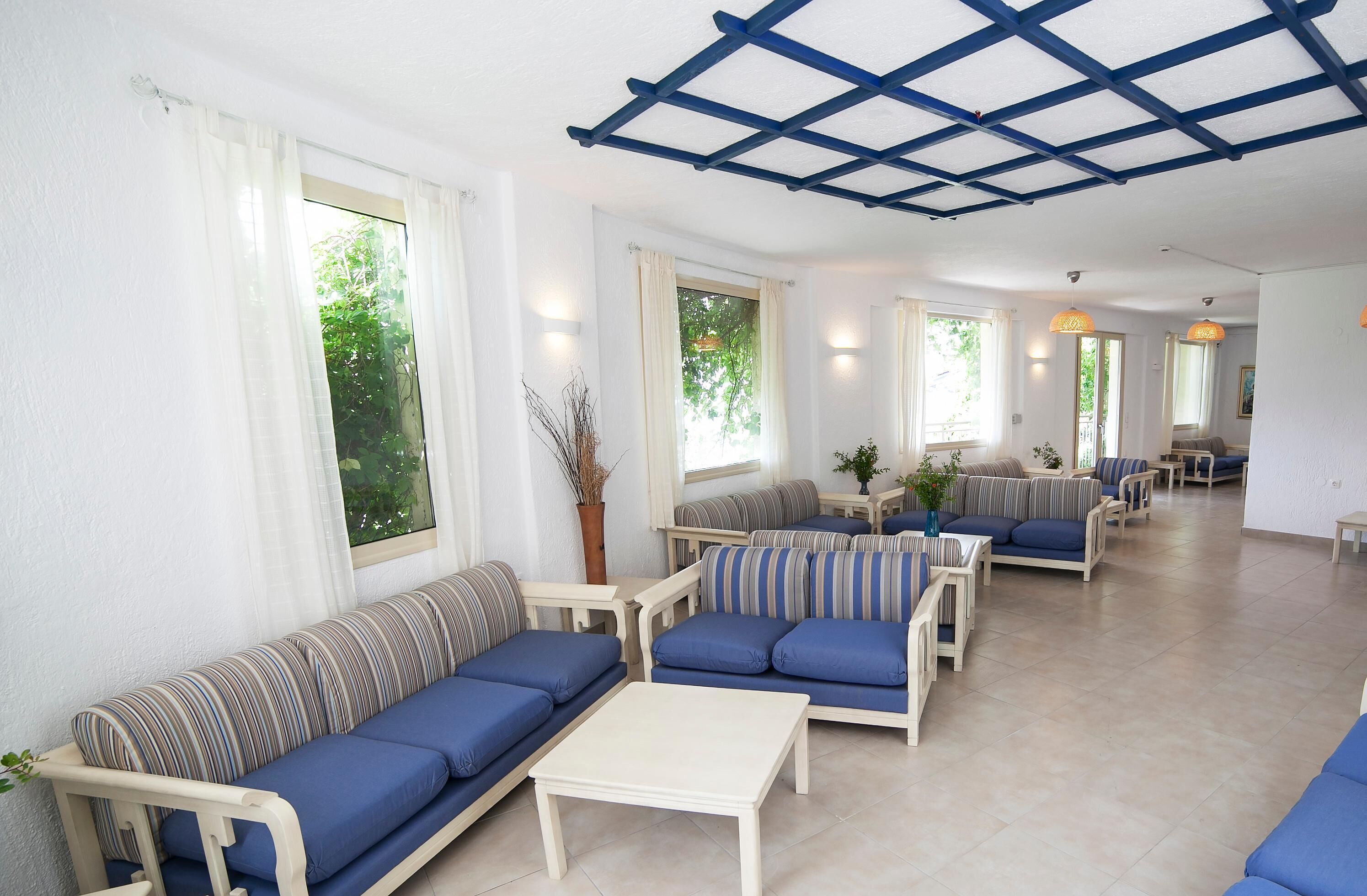 A spacious living area with multiple sofas and a coffee table, large windows with curtains, and a blue ceiling structure.