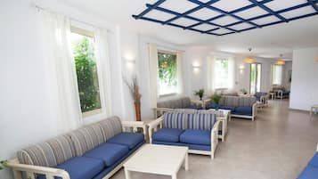 A spacious living area with multiple sofas and a coffee table, large windows with curtains, and a blue ceiling structure.