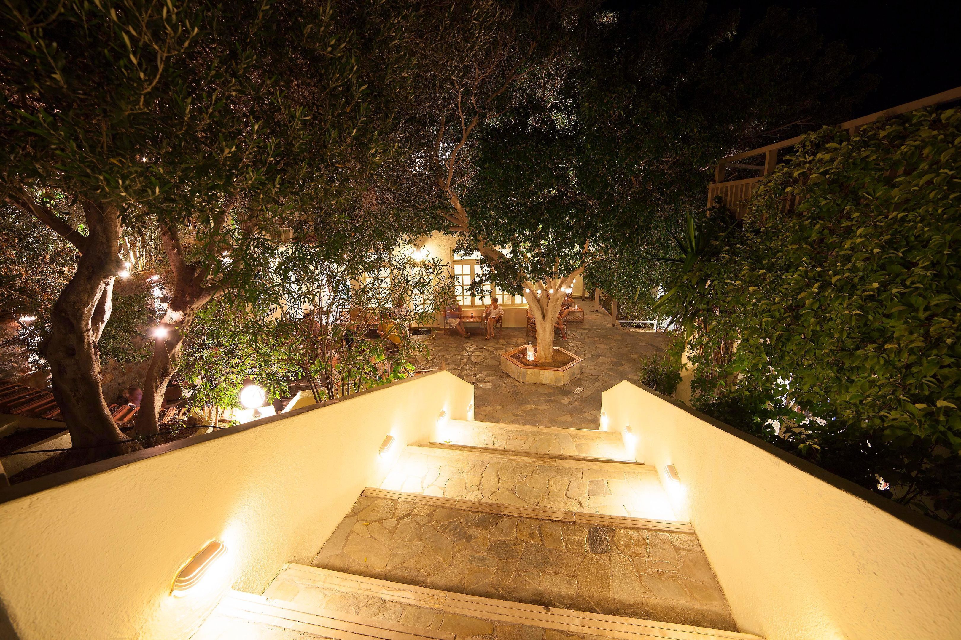 A nighttime view of a staircase leading to a building with a stone facade, surrounded by trees and illuminated by ambient lighting.