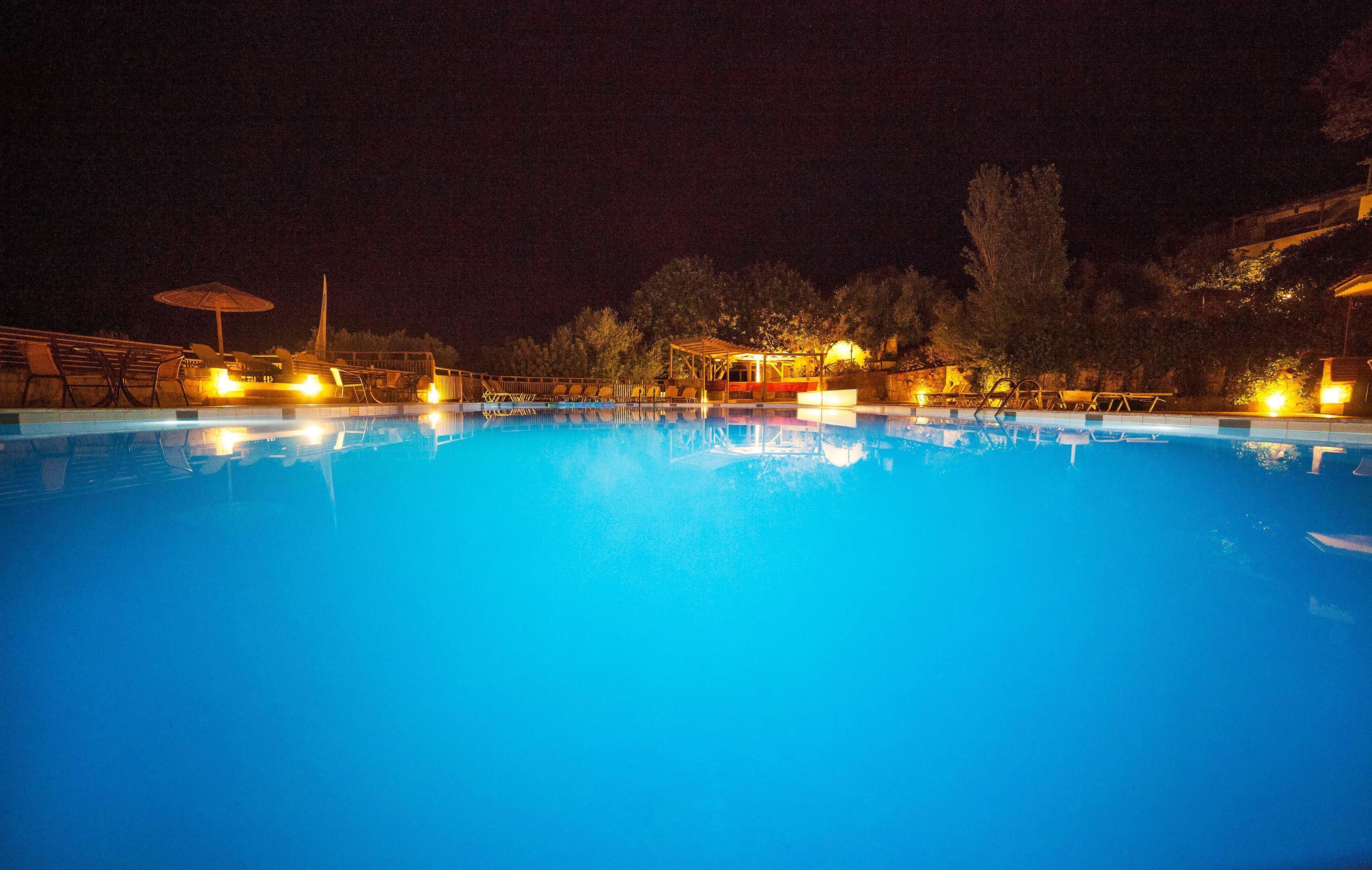 A nighttime swimming pool with clear water, surrounded by lounge chairs and umbrellas, and illuminated by ambient lighting.