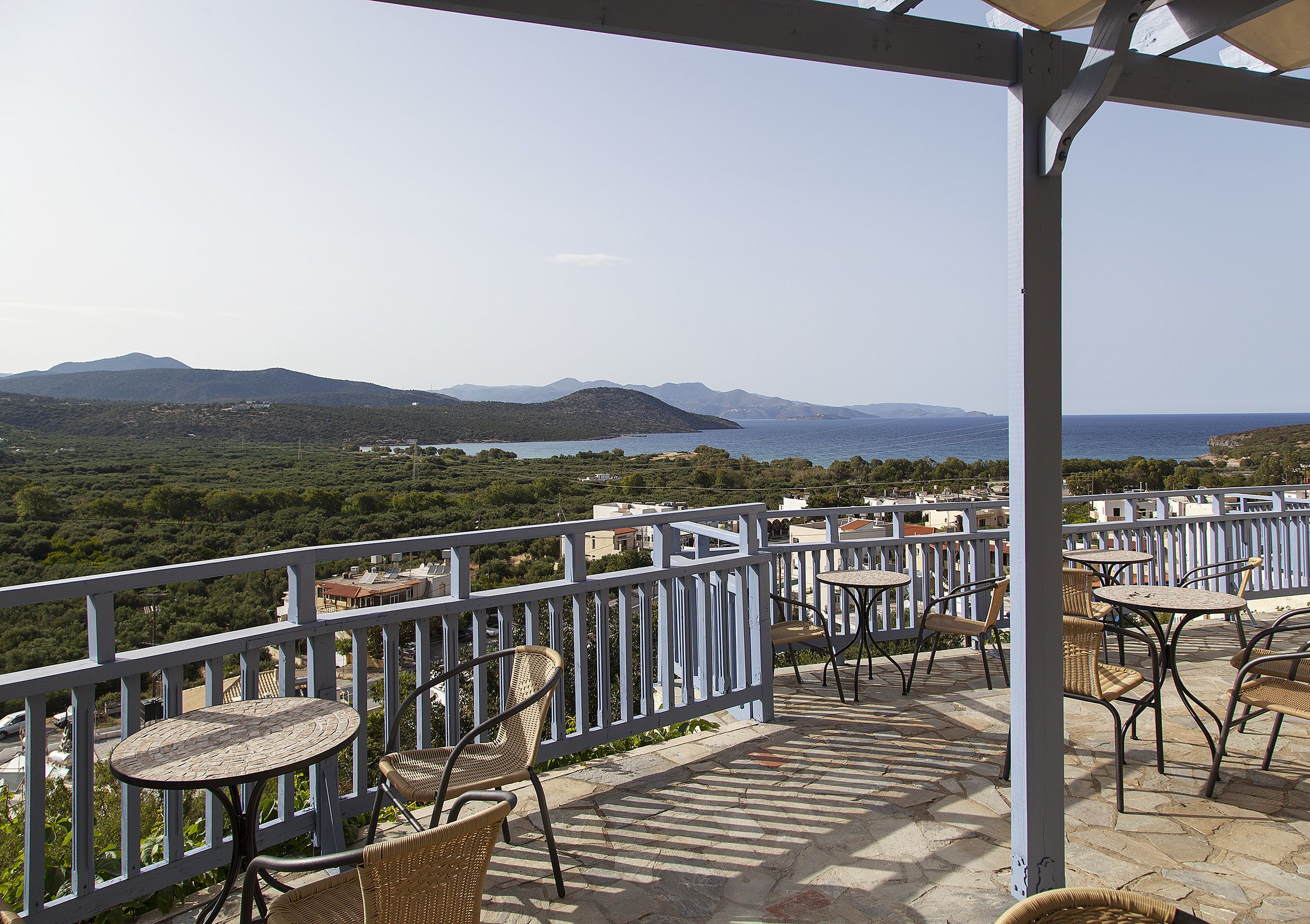 A terrace with tables and chairs overlooking a scenic landscape with mountains and a body of water.