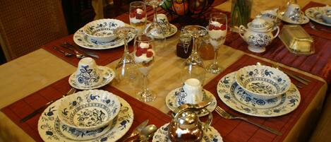 Una mesa de comedor dispuesta con platos blancos y azules estampados, cubiertos y una tetera de plata.