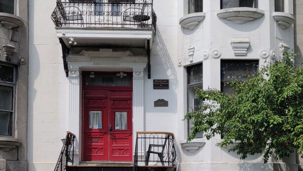 A Victorian-style building with a red door, a balcony, and a staircase leading to the entrance. - Gingerbread Manor (Montreal)