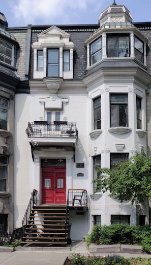 A Victorian-style building with a red door, a balcony, and a staircase leading to the entrance. - Gingerbread Manor (Montreal)