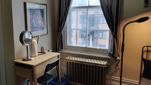 A room with a desk, a radiator, a window with curtains, a framed picture on the wall, and a floor lamp. - Gingerbread Manor (Montreal)