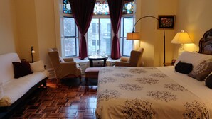 A hotel room with a large bed, two armchairs, a small table, and a window with stained glass. - Gingerbread Manor (Montreal)
