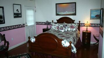 Een slaapkamer met een houten bed, bloemenbeddengoed, een nachtkastje met een lamp en een raam met jaloezieën.