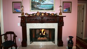A fireplace with a fire, a chair, and two framed paintings on the wall. - Heron Cay Lakeview Bed & Breakfast Inn (Mount Dora)