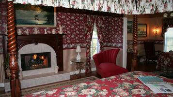 Un dormitorio con chimenea, papel tapiz floral, un sillón rojo y una cama con colcha estampada.