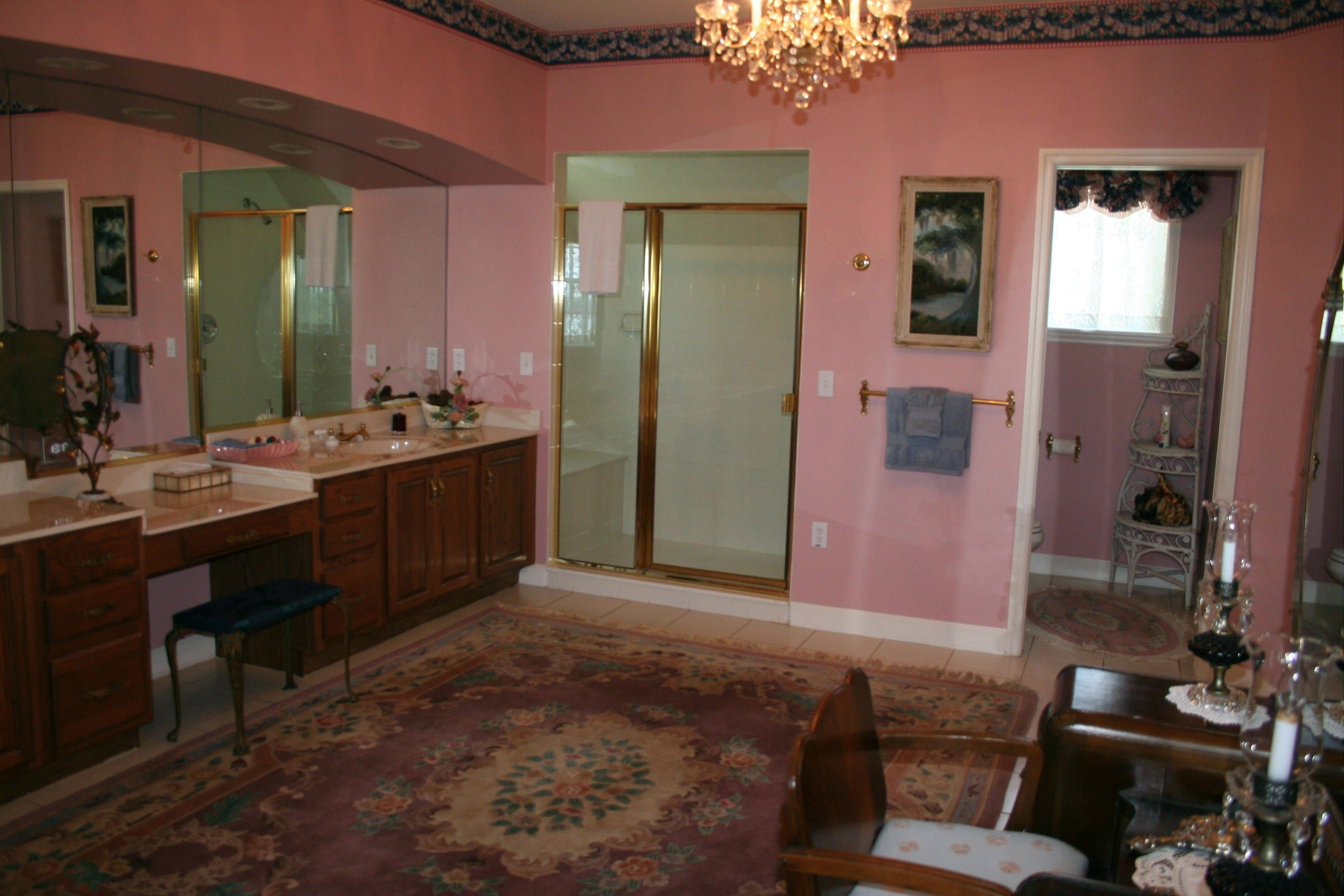 A pink-walled bathroom with a large mirror, a shower, and a vanity with a sink.