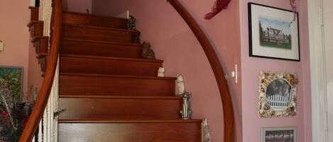 A wooden staircase with white balusters, a pink wall with framed pictures, and a vase with flowers on the landing.