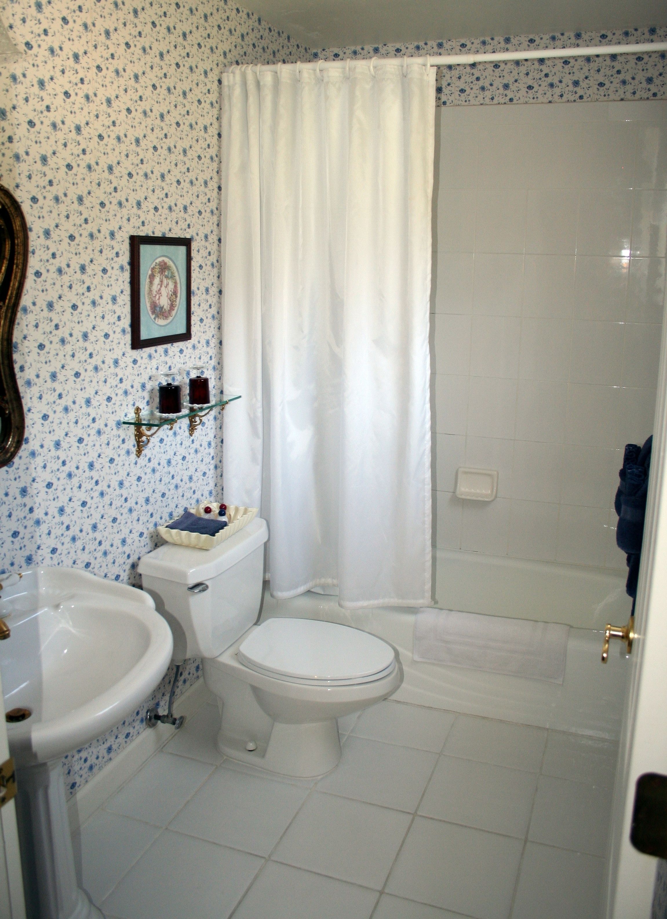 A bathroom with a toilet, sink, shower, and a framed picture on the wall.