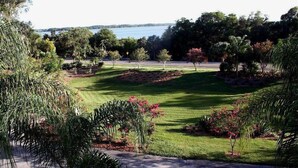 A well-maintained lawn with a variety of trees and shrubs, a clear view of a body of water, and a paved path. - Heron Cay Lakeview Bed & Breakfast Inn (Mount Dora)